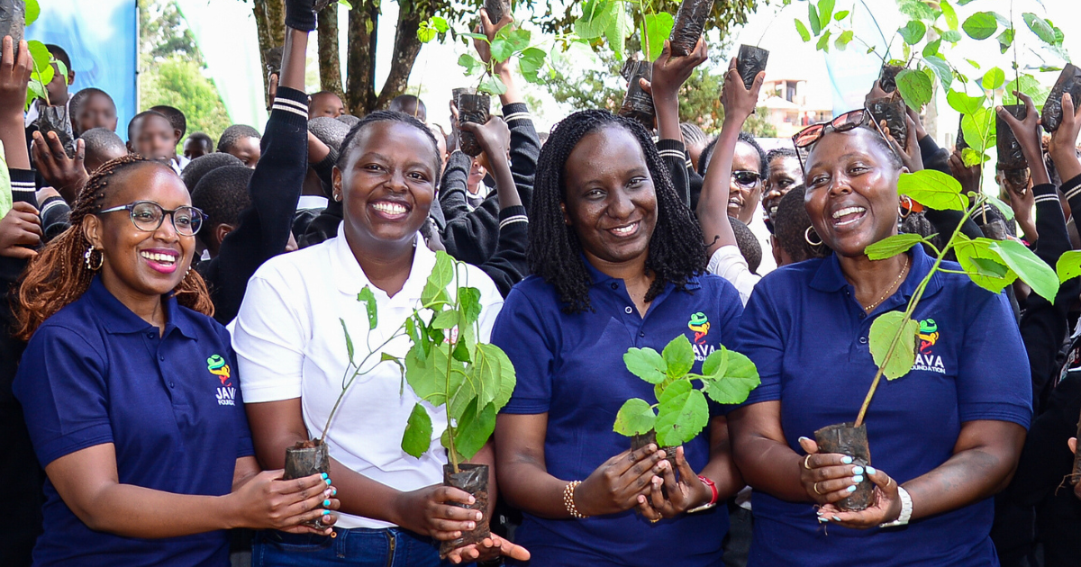 Java House Foundation team all smiles holding tree seedlings with Manguo primary school students in the back | Trees for Tomorrow Initiative by Java House Africa